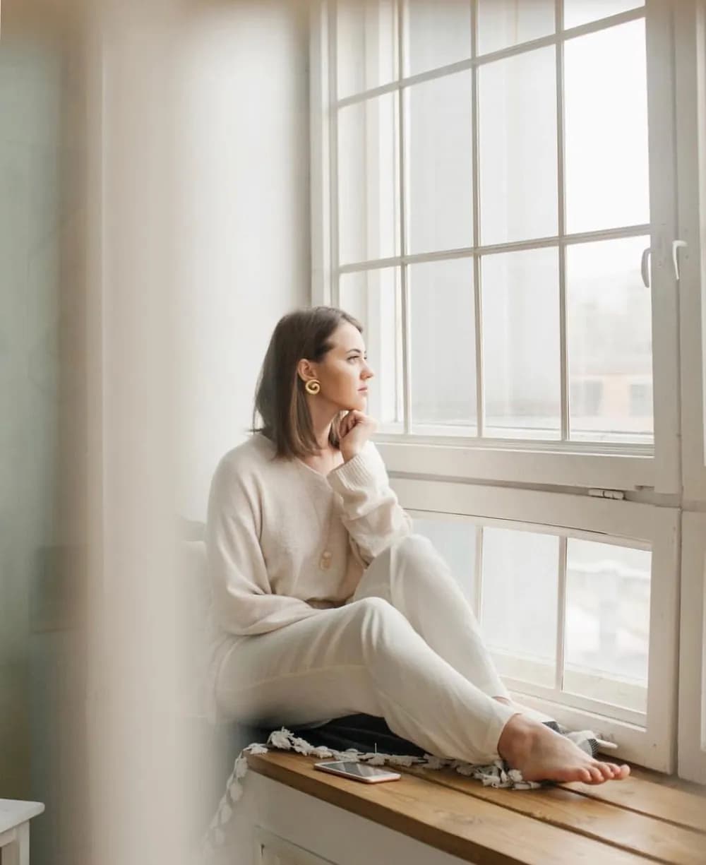 A woman sitting by a bright window, lost in thought